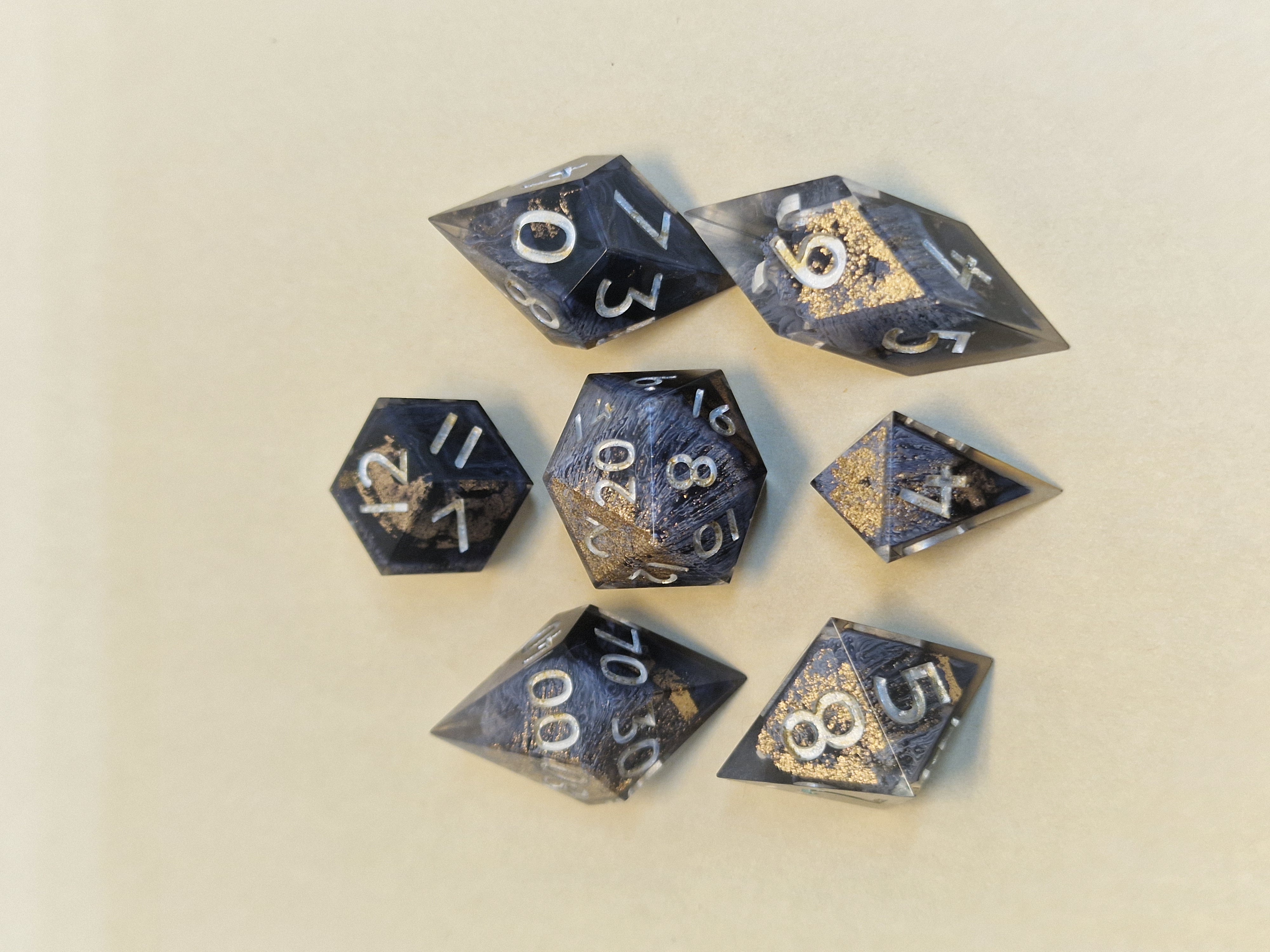 Wisps of smoky grey curl through dark resin, scattered with gold-toned flecks and silver numbers.
