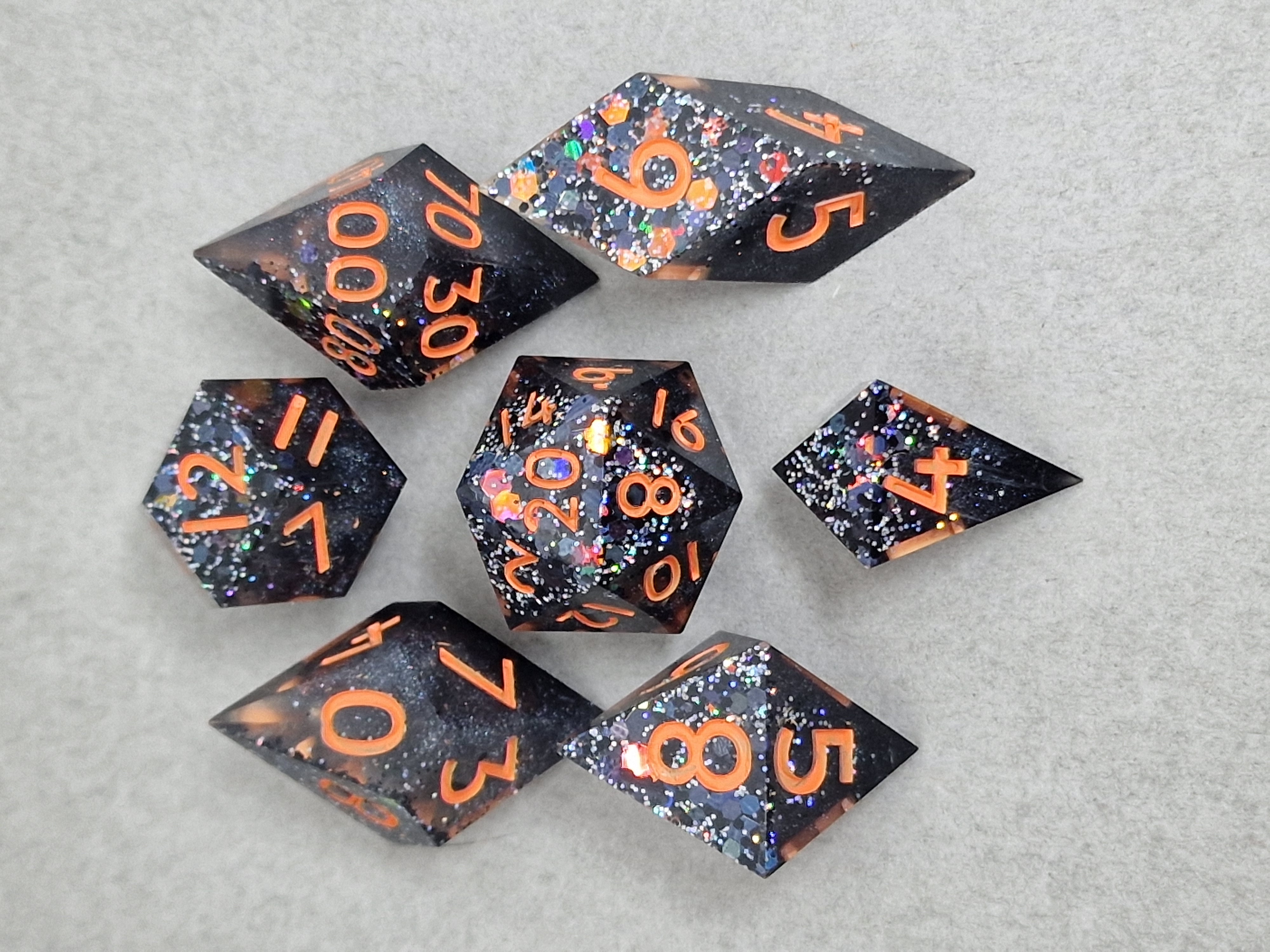 Black glitter and colourful flashes brew beneath vivid orange numbers in these pointed dice.